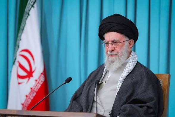 Ayatollah Ali Khamenei, head of state and Commander-in-Chief of Iran, seated before the Iranian flag